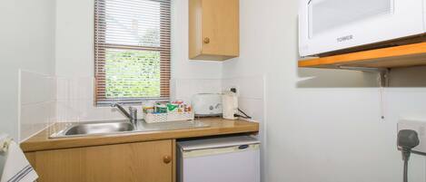 A compact kitchen with a sink, a toaster, a refrigerator, and a window with blinds.