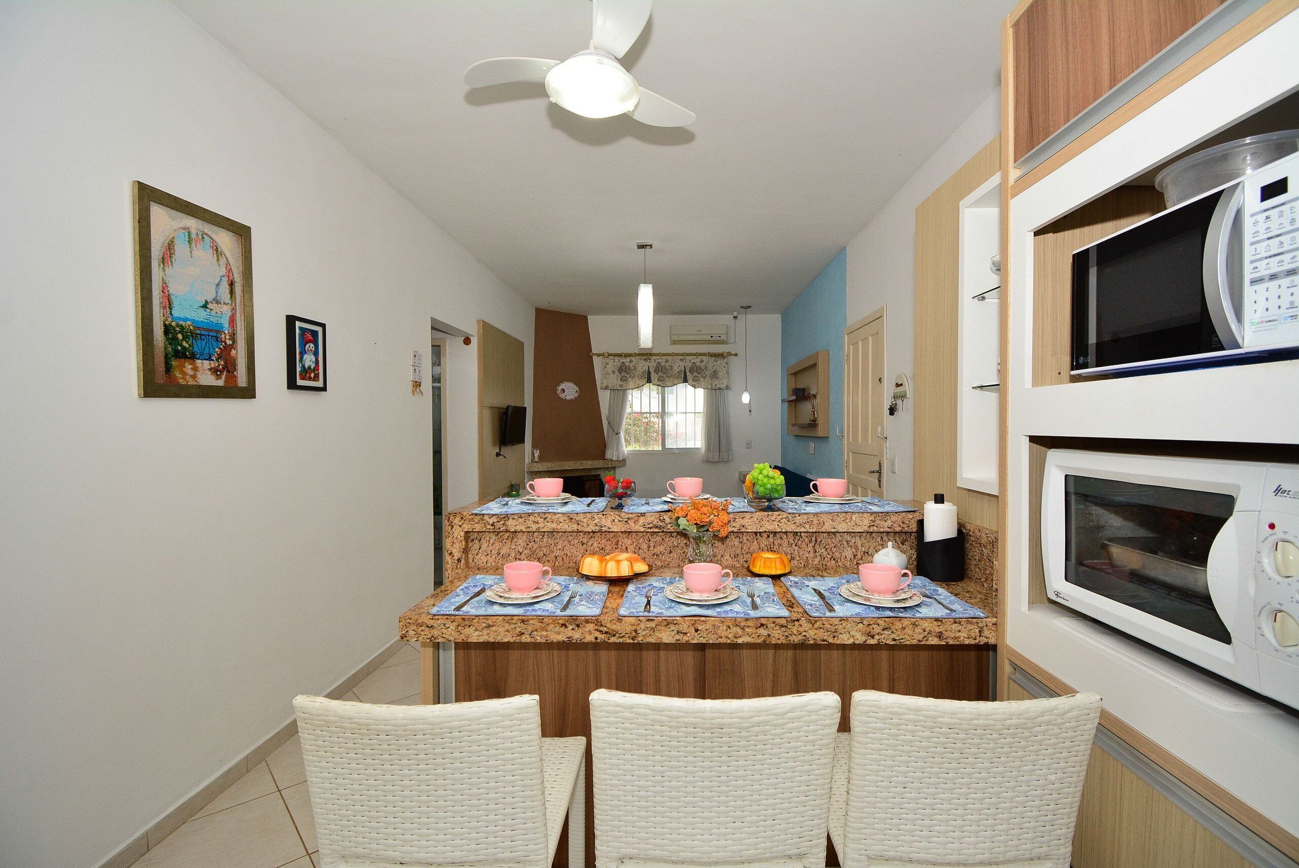 Una cocina con microondas, ventilador de techo y comedor con sillas y mesa para dos.