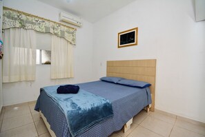 A bedroom with a bed, a window with curtains, an air conditioning unit, and a framed picture on the wall.