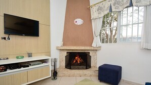 Una sala de estar con una televisión de pantalla plana, una chimenea, un otoman azul y una mesa de centro.