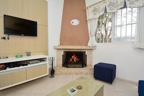 A living room with a flat-screen TV, a fireplace, a blue ottoman, and a coffee table. - Casa Aconchegante na Lagoa da Cigana (Laguna)