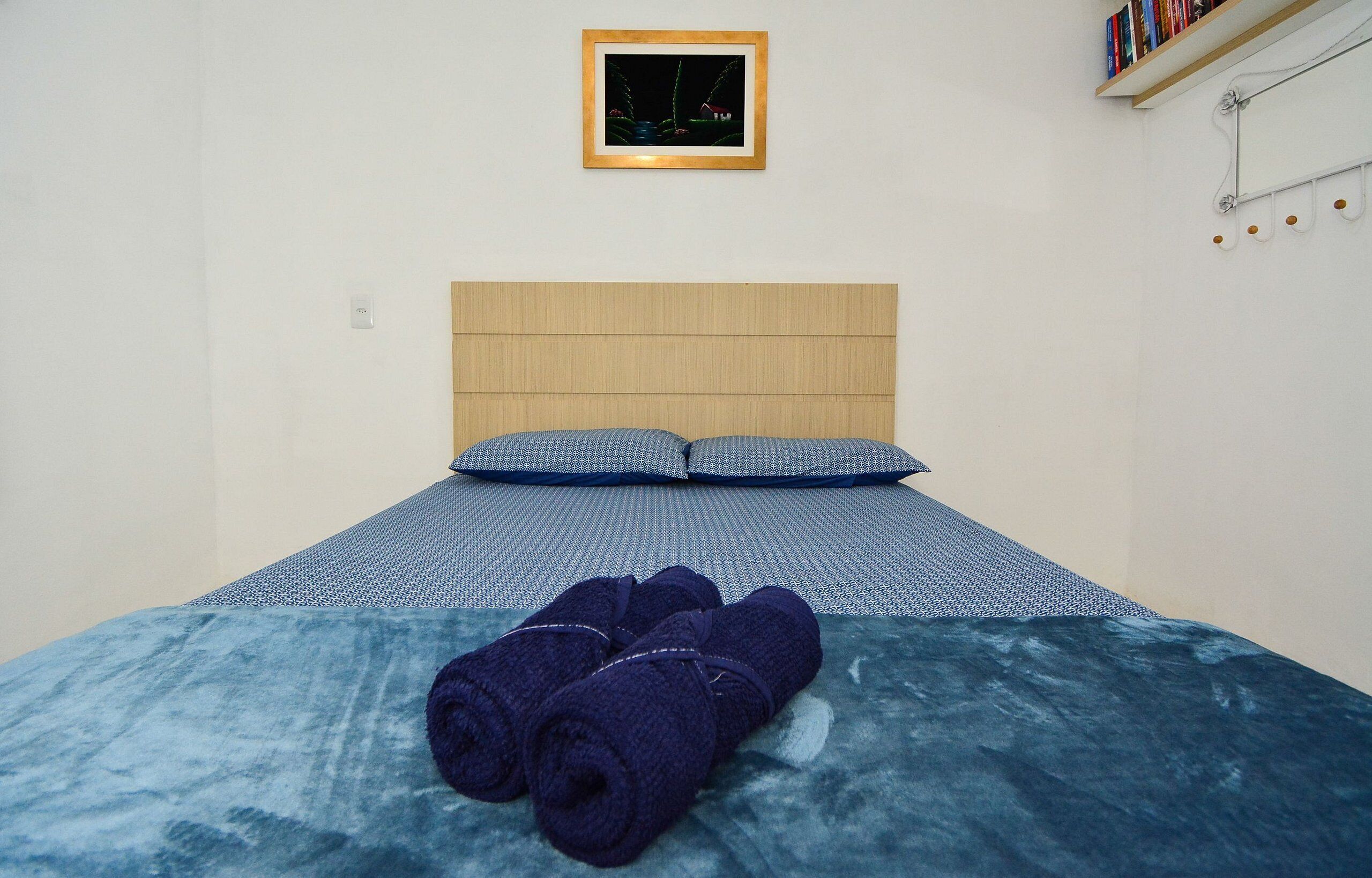 Un dormitorio con cabecera de madera, dos almohadas, una colcha azul y toallas enrolladas sobre la cama.