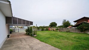 Una propiedad residencial con camino de entrada pavimentado, césped y un edificio rojo al fondo.