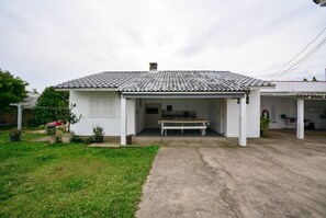 Uma casa branca com telhado de telhas, alpendre coberto e um pequeno jardim.