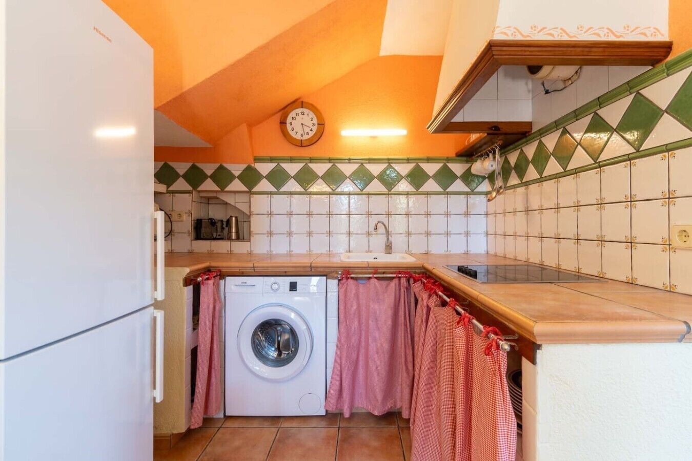 A compact kitchen with a washing machine, a clock, and a tiled backsplash.