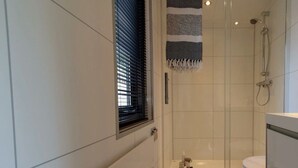 Ein modernes Badezimmer mit Duschkabine aus Glas, Toilette und Fenster mit Jalousien.
