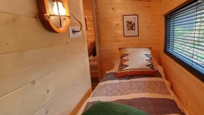 Ein Holzblock-Innenraum mit einem Bett, einer Wandleuchte und einem Fenster mit Jalousien.