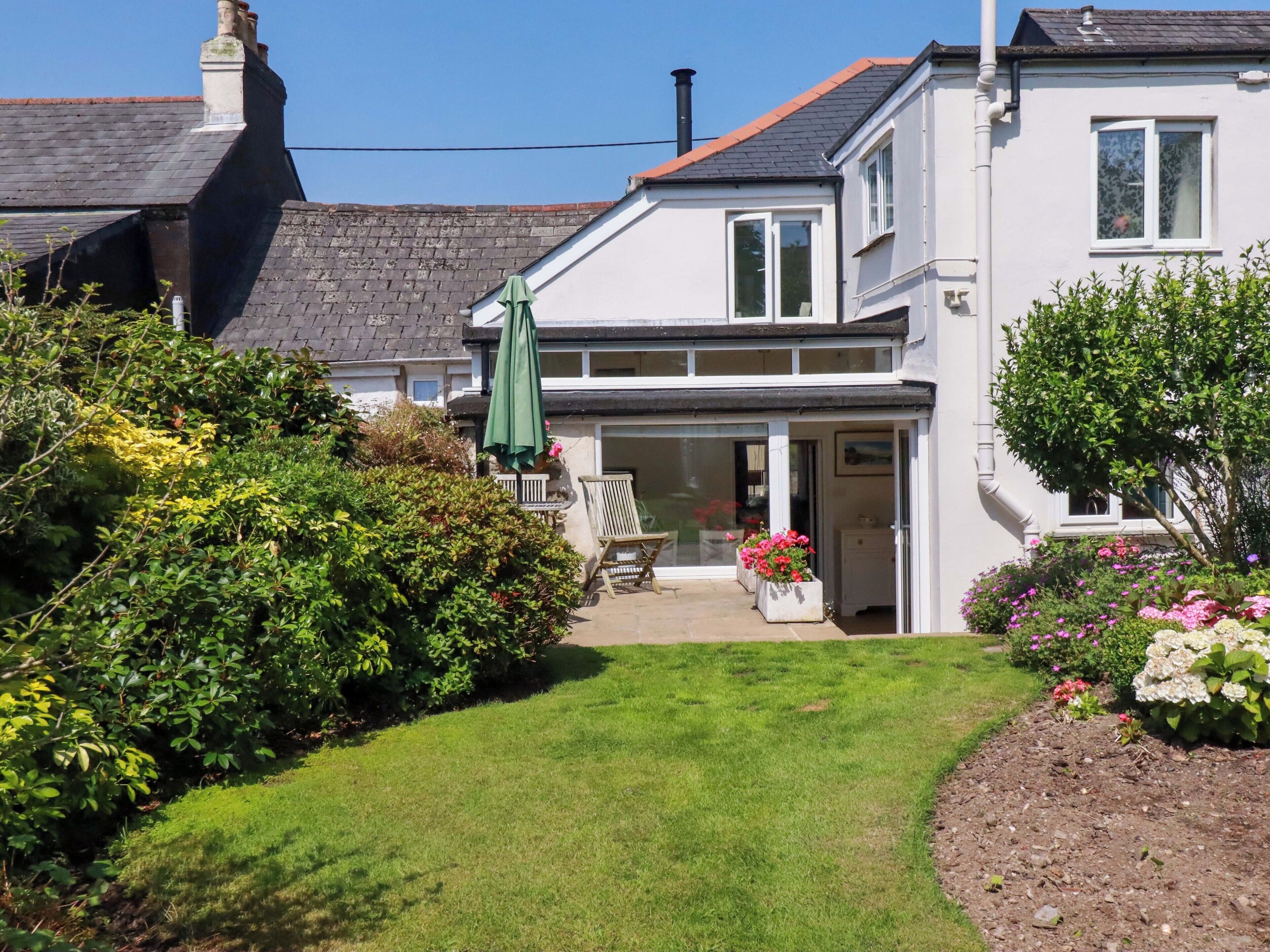 A two-story house with a front garden, a green umbrella, and a white exterior.