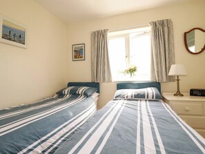 A bedroom with two beds, a window with curtains, a bedside table with a lamp, and a wall-mounted mirror. - Marys House (Falmouth)