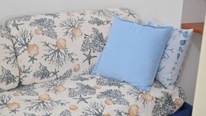 Un canapé recouvert d’un tissu à motifs marins et agrémenté d’un seul coussin bleu.