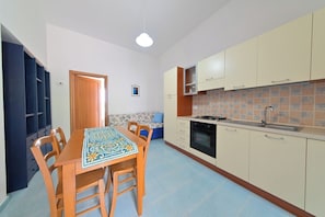 A compact kitchen with a dining table, chairs, a stove, and cabinets. - Breeze (Barano D'ischia)
