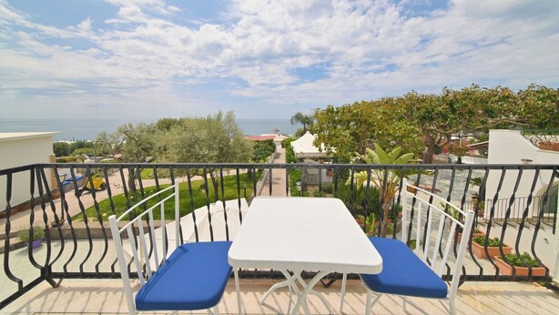 Un balcon avec une table blanche et des coussins bleus, donnant sur un quartier résidentiel et offrant une vue sur la mer.