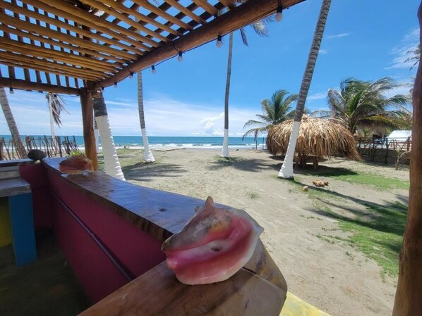 A beach view with a wooden pergola, palm trees, and a thatched structure.