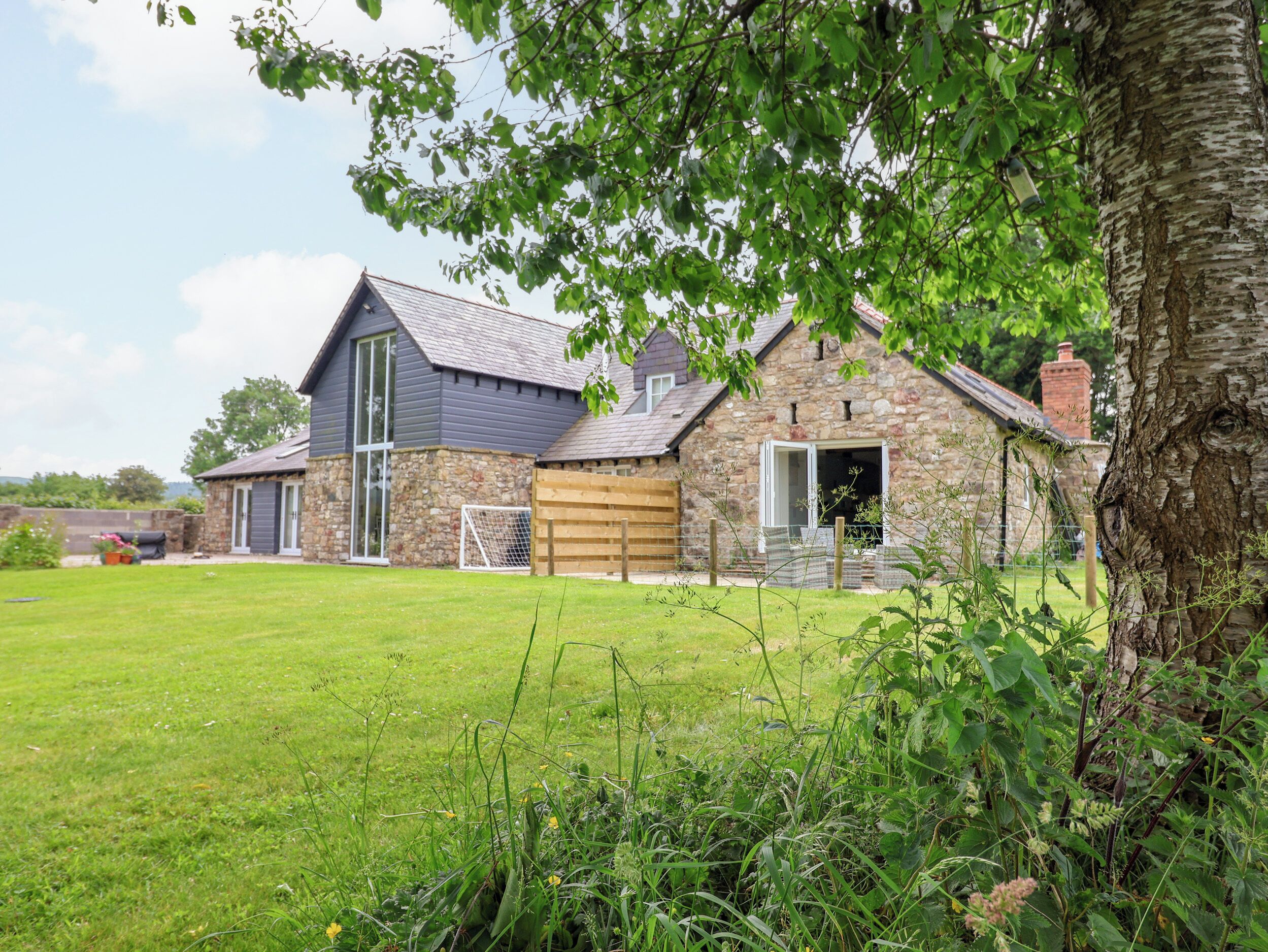 Une maison en pierre avec un grand garage, une cour verdoyante et un arbre au premier plan.