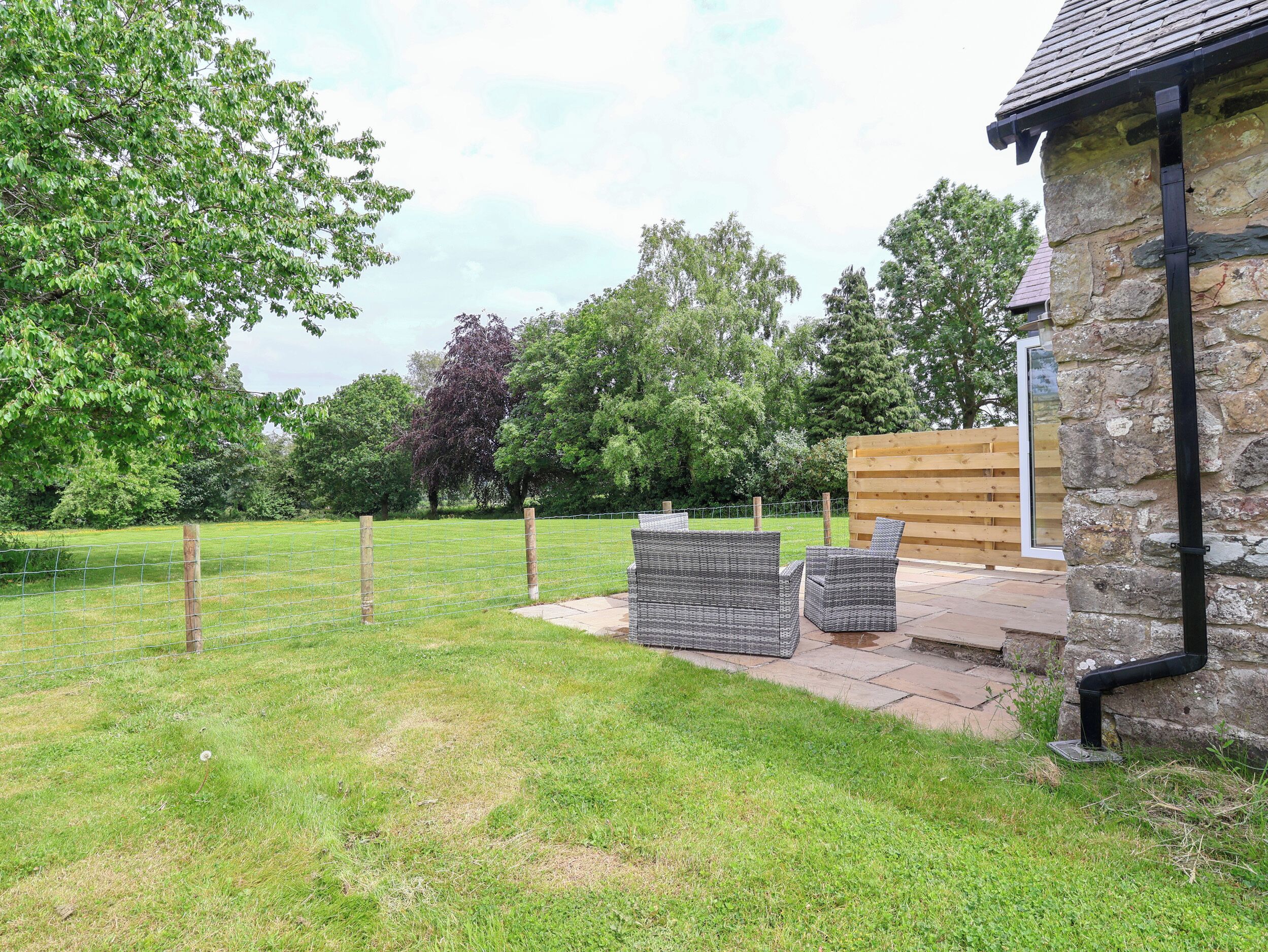 A stone building with a wooden deck, wicker furniture, and a fenced garden area.