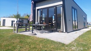 A modern building with large glass doors, a patio with a grill, and a clear sky. - Just Nature Light 4 (Kampen)