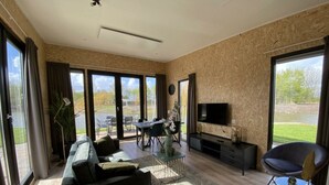 A spacious living room with a sofa, TV, and dining area, large windows, and a view of the outdoors. - Just Nature Light 4 (Kampen)