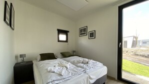 A bedroom with a bed, two bedside tables, a window, and a door leading to a balcony. - Just Nature Light 4 (Kampen)