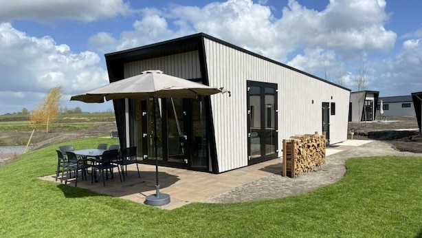 A modern building with a patio area, outdoor seating, and a stack of firewood. - Just Nature Light 4 (Kampen)
