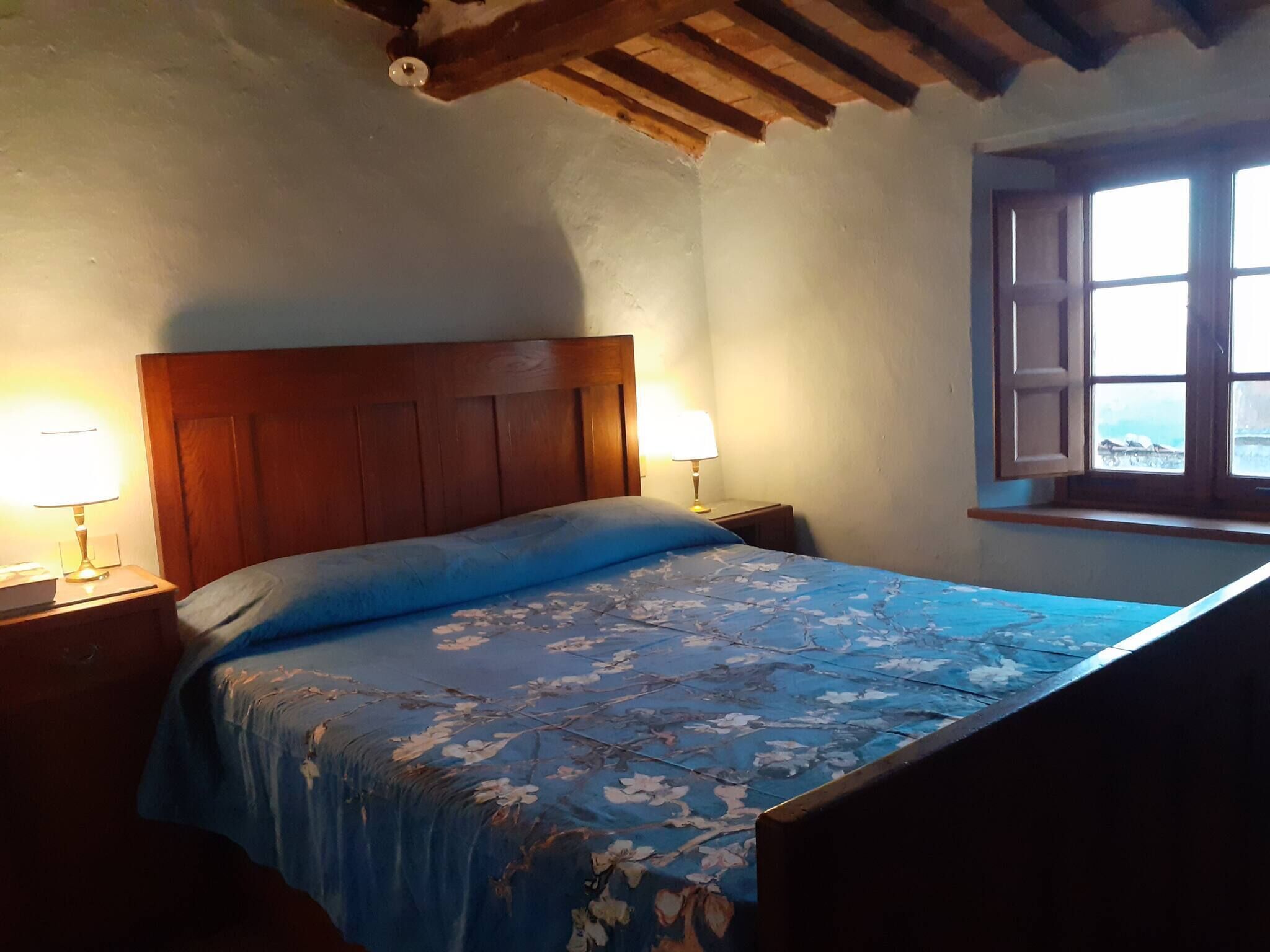 Une chambre à coucher avec une tête de lit en bois, deux lampes de chevet, une fenêtre donnant sur un beau paysage et une couvre-lit à motifs floraux.
