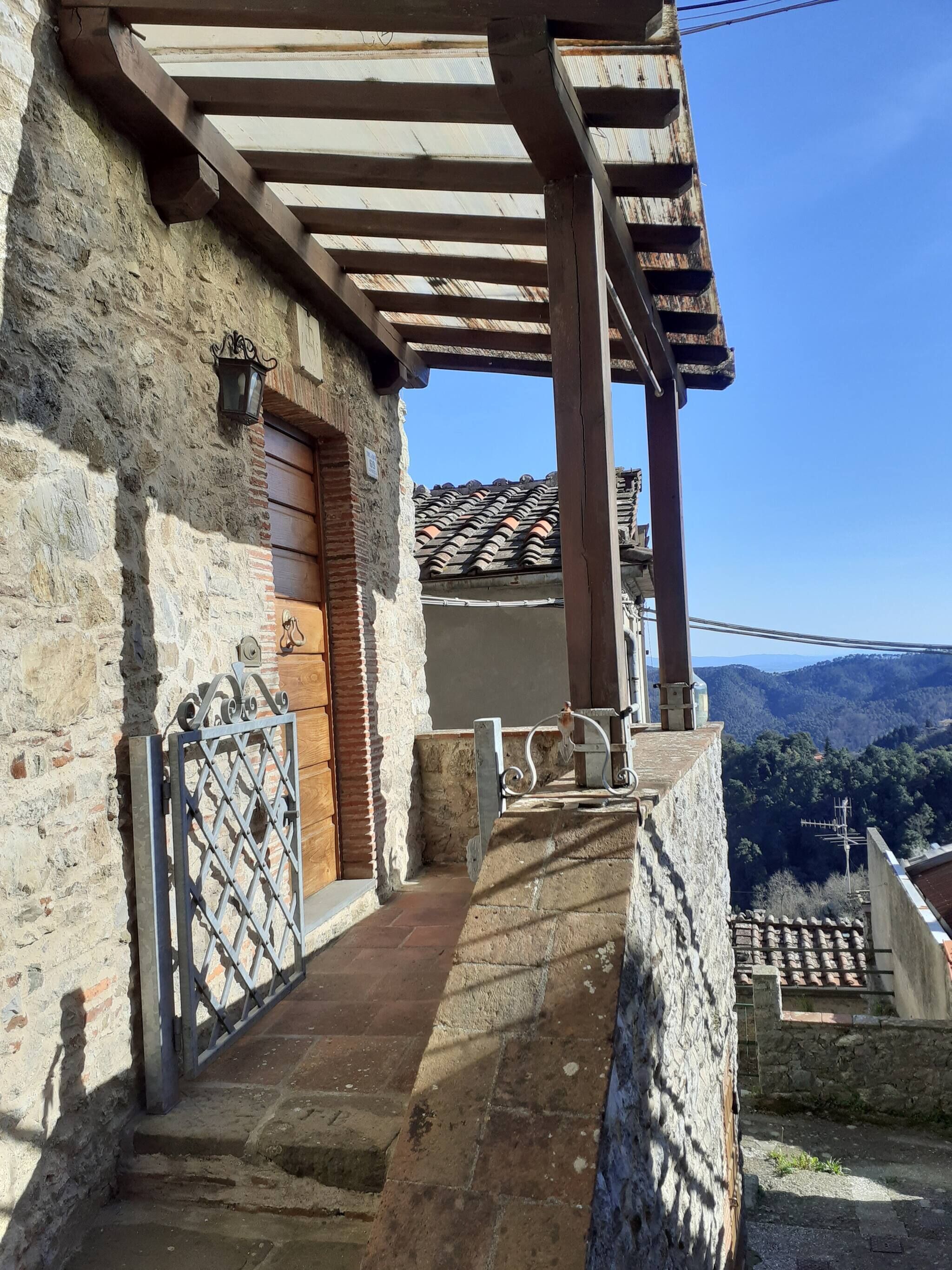 A stone building with a wooden door, a metal gate, and a view of a hilly landscape.