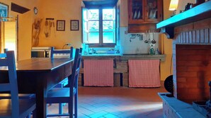 Une cuisine rustique avec une table en bois, des chaises, une fenêtre et une cheminée en briques.