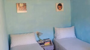 Une chambre avec deux lits, une table de chevet avec des livres, une lampe et deux éléments de décoration murale.
