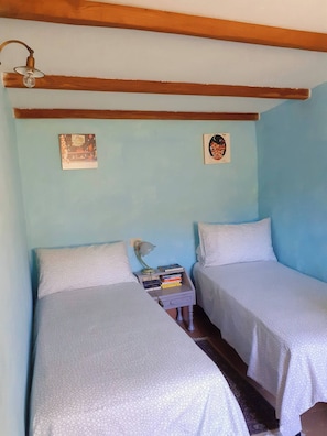 Ein Zimmer mit zwei Betten, einem Nachttisch mit Büchern, einer Lampe und zwei Wandbildern.