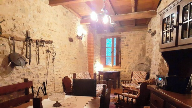 Une pièce rustique aux murs de pierre, avec des meubles en bois, une table recouverte d’une nappe en dentelle et une radio.