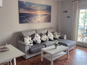 Ein Wohnzimmer mit grauem Sofa, weißem Couchtisch und einem Gemälde vom Sonnenuntergang über dem Meer.