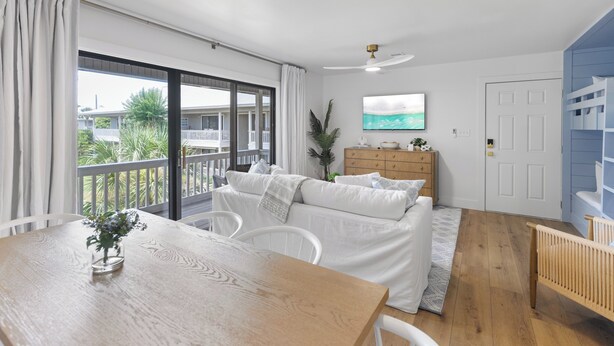 A room with a balcony, a sofa, a wooden table, a TV, and a door. - My Blue Heaven 30A Getaway - Beach Access, Pools & Prime 30A Location (Santa Rosa Beach)