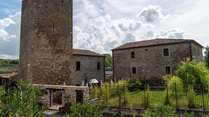 Un edificio histórico de piedra con una torre, estructuras más pequeñas adyacentes y un jardín cercado.