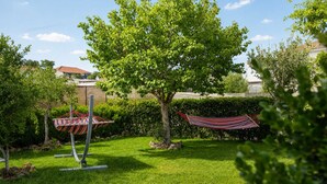 Un espacio al aire libre con césped, una hamaca, una escultura de metal y un árbol.