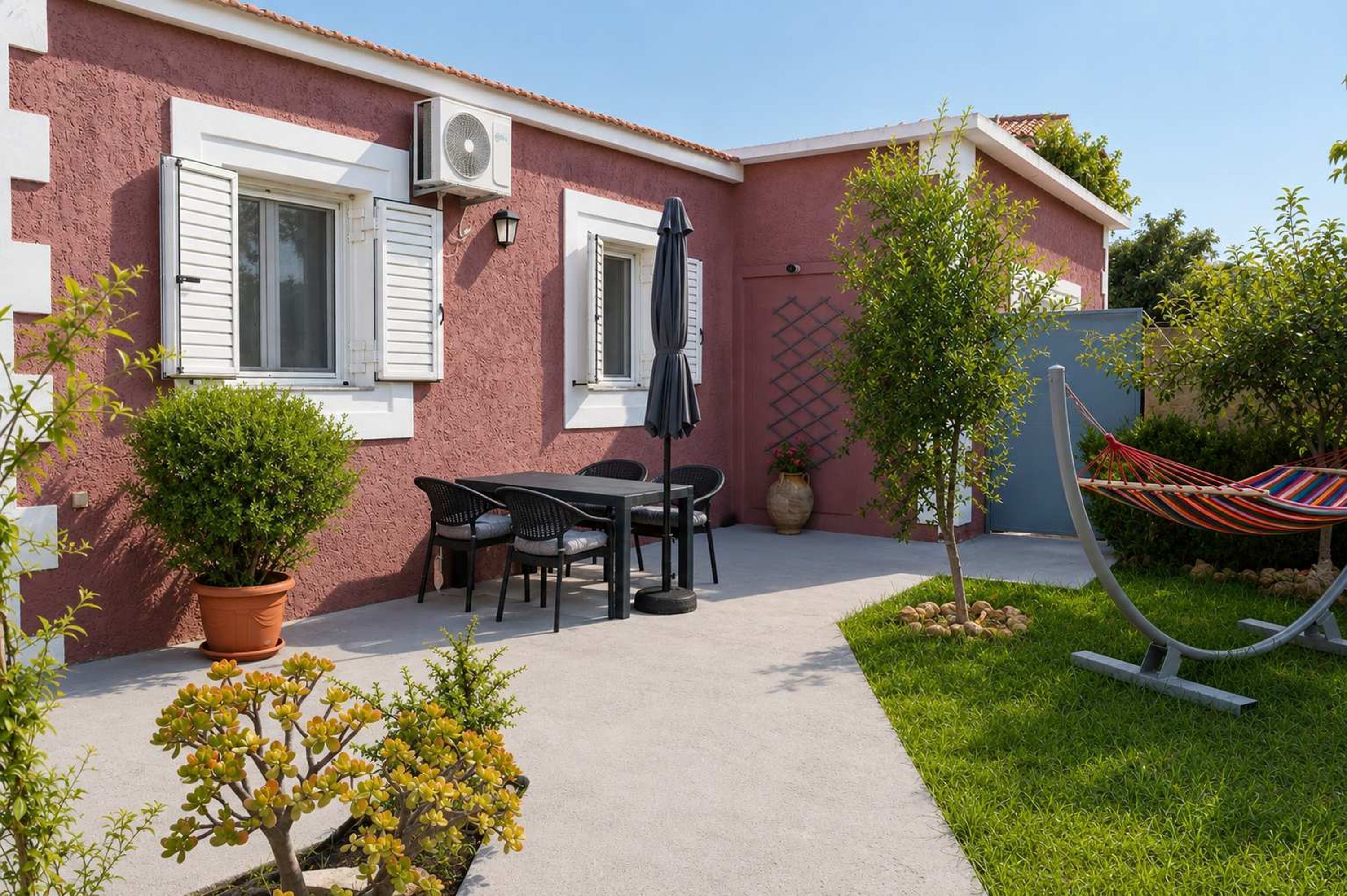 A house with a patio, a table with chairs, a hammock, and a potted plant.