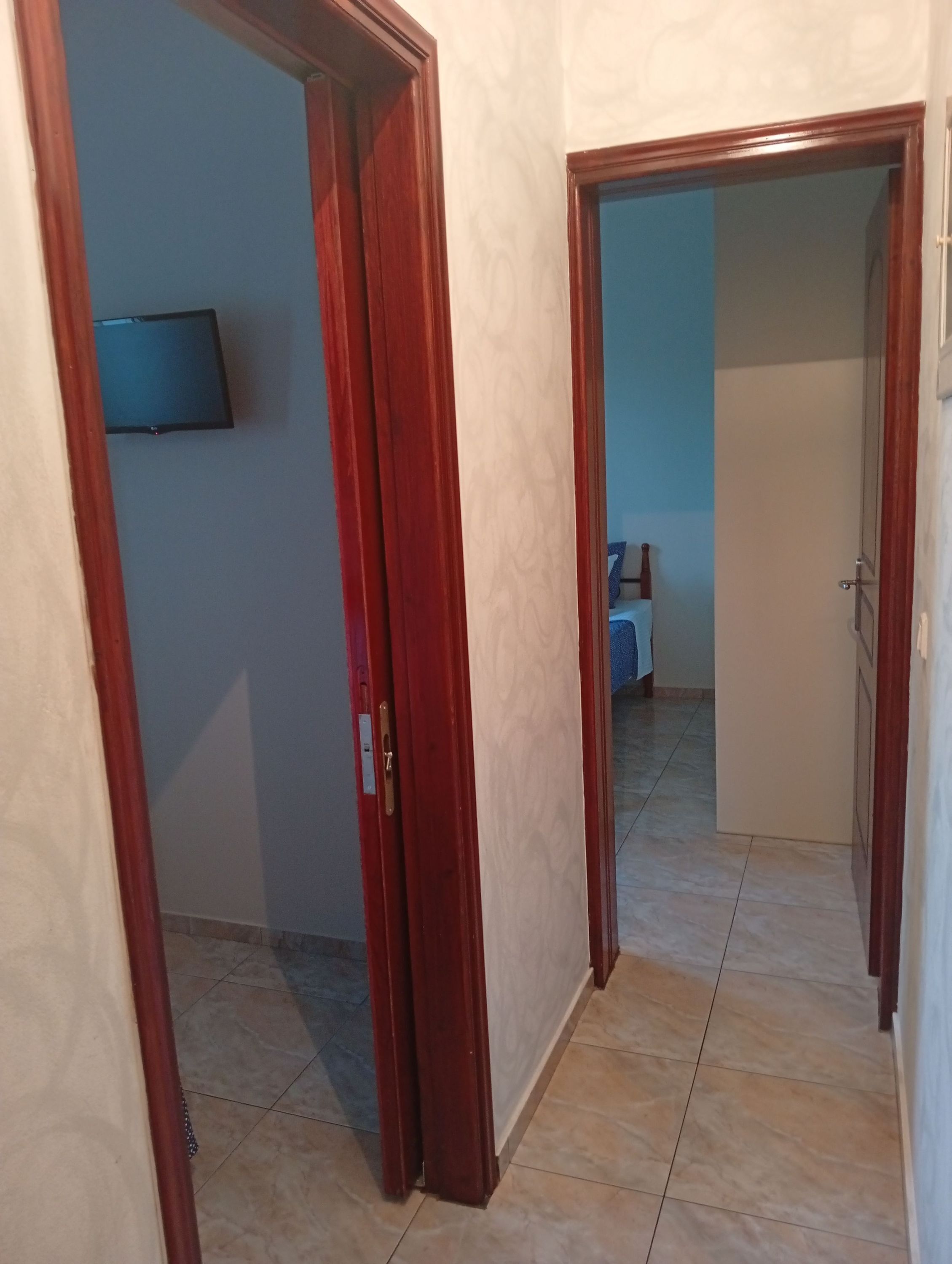 Un pasillo con una puerta de madera, suelo de baldosas y un televisor colocado en la pared.