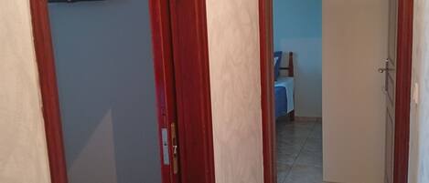 Un pasillo con una puerta de madera, suelo de baldosas y un televisor colocado en la pared.