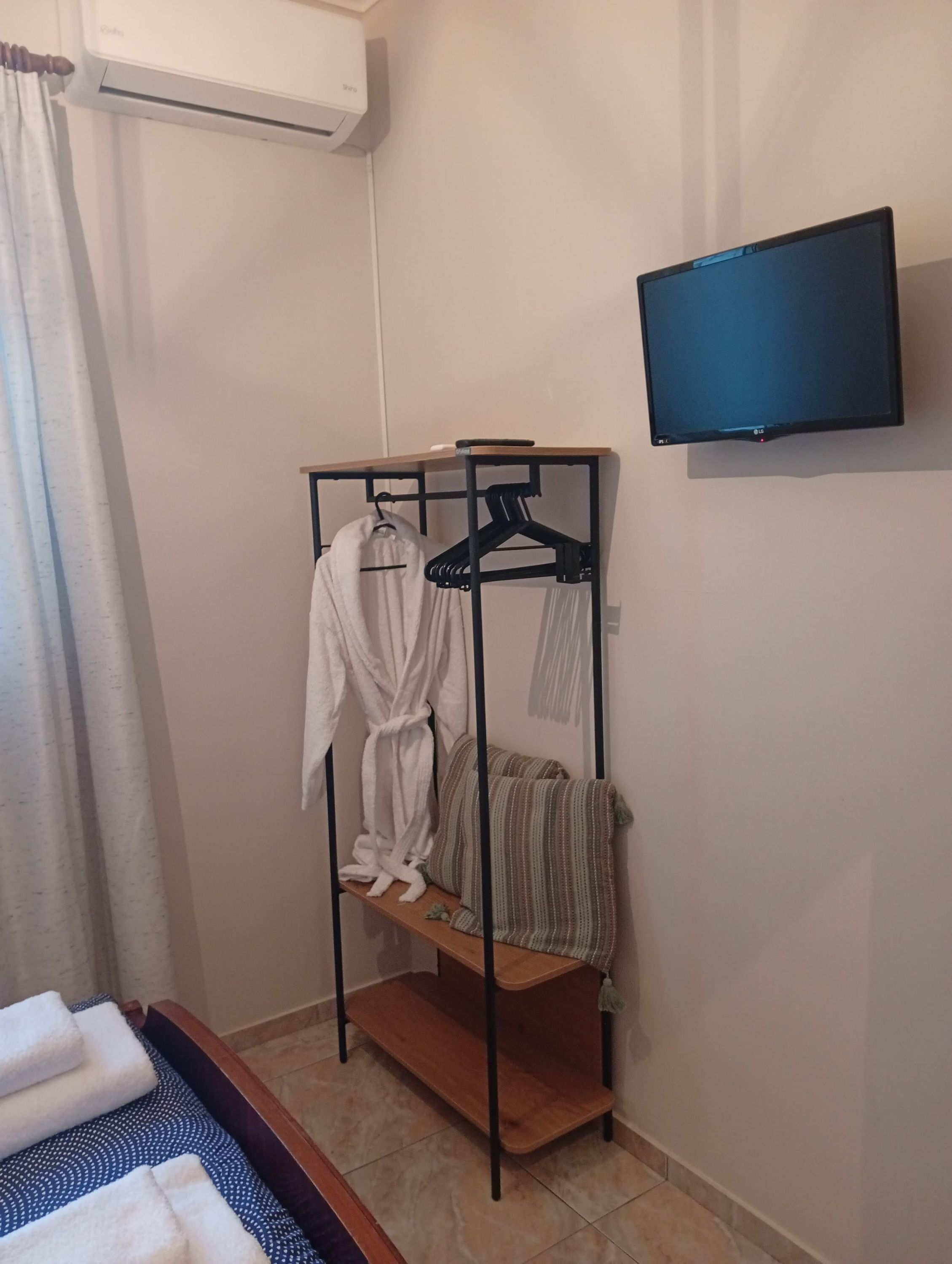 Habitación de hotel con una cama, estante de madera, perchero, televisión y cortina.