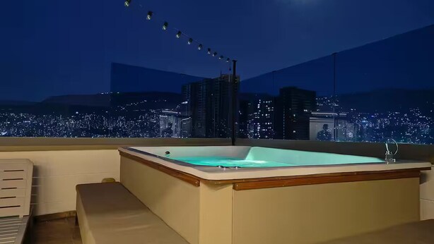 Eine Dachterrasse mit Whirlpool, Sitzgelegenheit und Blick auf die nächtliche Stadt.