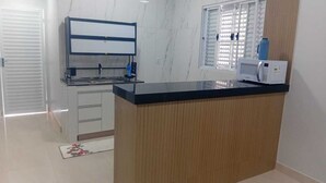 Una cocina con encimera negra, armarios blancos, microondas y una ventana con persianas.