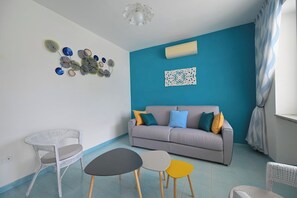 A living room with a grey sofa, colorful cushions, a white chair, a small round table, and decorative wall art. - Armonia (Barano D'ischia)