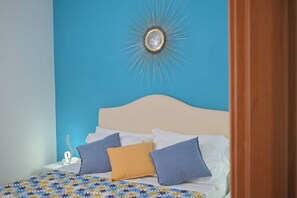 Ein Bett mit einem gemusterten Überwurf, einem weißen Kopfteil und mehreren Kissen in verschiedenen Farben.