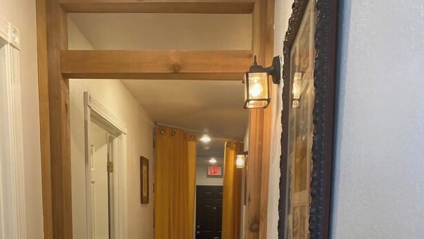 Un corridoio con travi in legno, una porta, un lampadario e un quadro appeso al muro.