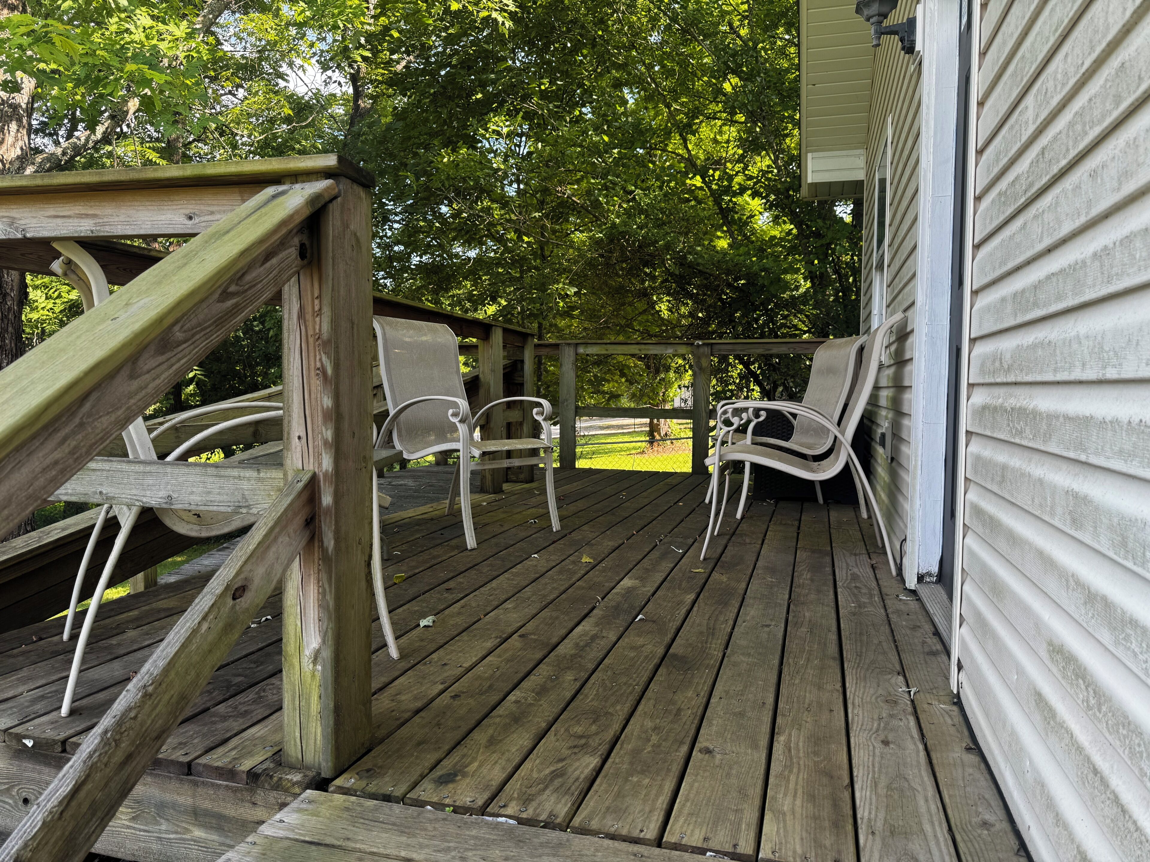 Une terrasse en bois avec deux chaises blanches et une rambarde en bois.