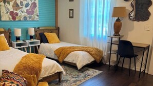 Una camera d'albergo con due letti, una scrivania, una sedia, una sveglia e un quadro floreale appeso al muro.