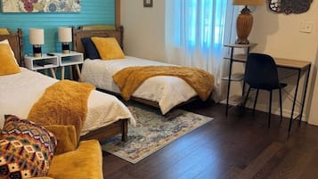 Une chambre d’hôtel avec deux lits, un bureau, une chaise, une horloge et une œuvre d’art florale accrochée au mur.