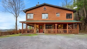 A two-story log cabin with a porch, a satellite dish, and a stone wall. - Mountain Getaway with Big Views, 3 King Beds, Game Room, Hot Tub, Pet Friendly! (Sevierville)