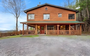 A two-story log cabin with a porch, a satellite dish, and a stone wall.