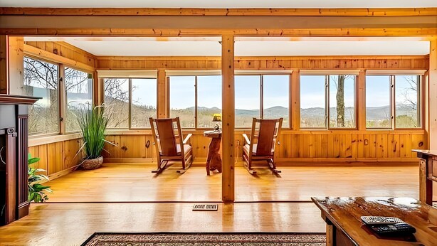 A spacious room with wooden walls and large windows, a fireplace, and a view of the mountains. - Mountain Getaway with Big Views, 3 King Beds, Game Room, Hot Tub, Pet Friendly! (Sevierville)