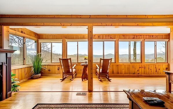 A spacious room with wooden walls and large windows, a fireplace, and a view of the mountains.
