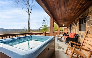 A hot tub on a wooden deck with stone walls, outdoor furniture, and a view of the landscape.